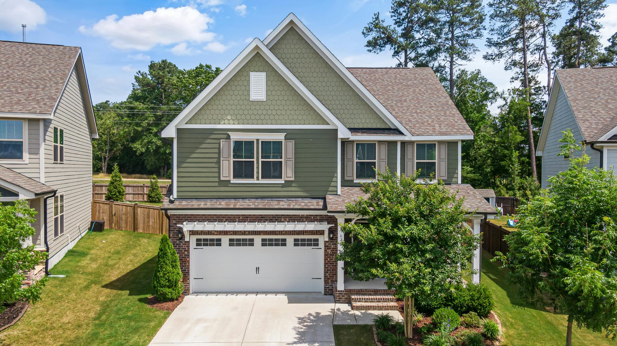 Aerial view of a modern green suburban home with a neatly landscaped front yard and garage in Wendell, NC.