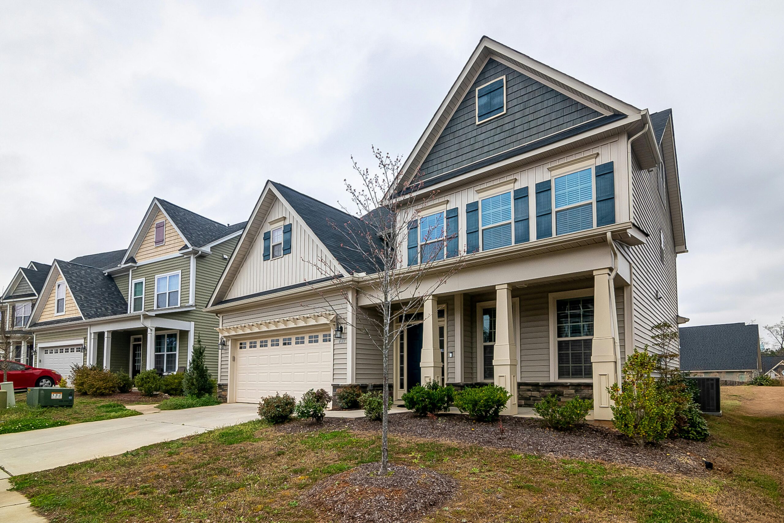 A row of modern suburban homes with garages, driveways, and landscaped lawns in daylight.