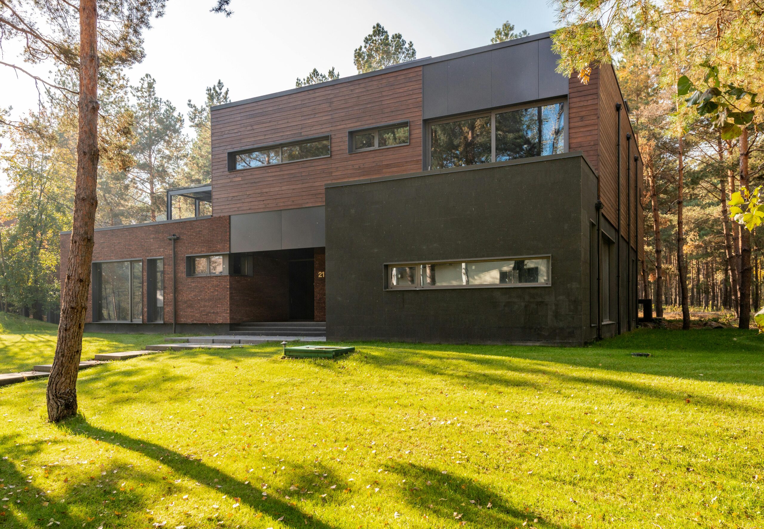 A modern two-story house with glass windows nestled in a forested area.